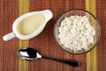 Sauce boat with condensed milk, bowl with grainy cottage cheese, spoon on mat. Top view Royalty Free Stock Photo