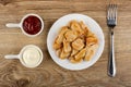 Sauce boats with ketchup and mayonnaise, white plate with pieces of fried chicken meat, fork on table. Top view