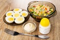 Saucer with halves boiled eggs, bowl with vegetable mix, bowl with mayonnaise, salt, fork on table