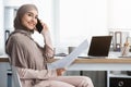 Saudi businesswoman working with documents and talking on cellphone in office