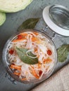 Sauerkraut with salt, sugar, carrots, dried viburnum and bay leaves in a glass jar on a concrete surface.