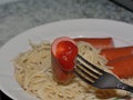 Sausage on a fork with ketchup close-up. Against the background of a plate of pasta Royalty Free Stock Photo