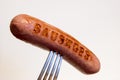 Sausage with an inscription pinned on a fork, on a white background.