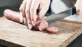 Sausage, knife, hands of woman, thick pieces, wooden plank, knife in female hands, woman cuts the sausage