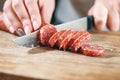 Sausage, knife, hands of woman, thick pieces, wooden plank, knife in female hands, woman cuts the sausage