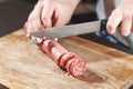 Sausage, knife, hands of woman, thick pieces, wooden plank, knife in female hands, woman cuts the sausage