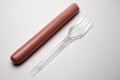 Sausage next to a plastic transparent fork on a white background. The concept of fast food, GMOs, hunger or lack of food.