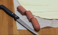 Sausage, puff pastry and knife on a wooden cutting board.