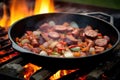 sausage slices sizzling in a campfire skillet