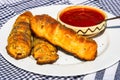 Sausages baked in dough sprinkled with salt and poppy seeds and bowl with tomatoes sauce in a rustic composition. Sausages rolls, Royalty Free Stock Photo