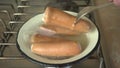 Sausages are boiled in a bowl on the stove, a fork pierces the sausage while boiling, boiling sausages