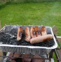 Sausages and burgers cooking on a disposable BBQ Barbeque in s garden Royalty Free Stock Photo