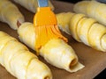 Sausages in the dough are prepared for baking. Brush the egg yolk. Close up.