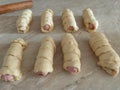 Sausages in the dough are prepared for baking. Tasty sausage rolls on the marble table. Raw hot dogs rolled in dough.