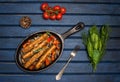 Sausages on the grill pan on blue background. Top view. Frying pan with fried sausage, tomatos, herbs and fork on wooden table