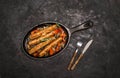 Sausages on the grill pan on dark background. Top view. Frying pan with fried sausage, vegetables and fork and knife on a black