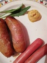 Sausages and hot dogs with mustard served on a plate and decorated with a few leaves arugula,top view from close up Royalty Free Stock Photo