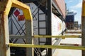 Secured white iso tank container on deck of container ship with red stickers indicated dangerous goods inside.