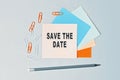 Save the date - text on sticky note paper on gray background. Closeup of a personal agenda. Top view Royalty Free Stock Photo