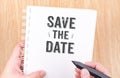 Save the date word on white ring binder notebook with hand holding pencil on wood table,Business concept