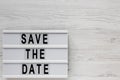 `Save the date` words on a lightbox on a white wooden background, top view. Overhead, from above, flat lay. Space for text