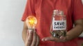 Save energy concept. Female hand holding a light bulb, coins in a jar with copy space Royalty Free Stock Photo