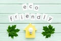 Green maple leaves, house, bulb and eco friendly text for ecology concept on mint green wooden background top view Royalty Free Stock Photo