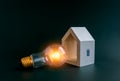 Saving energy, battery icon on white minimal wooden house with light bulb on dark blue background. Royalty Free Stock Photo