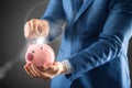 Saving money. Businesman holding pink piggy and putting coin into piggy bank Royalty Free Stock Photo