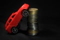 Saving money for a car. Banking, fast. Toy car and coins on black background. Miniature red car model on growing stack of coins. Royalty Free Stock Photo