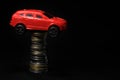 Saving money for a car. Banking, fast. Toy car and coins on black background. Miniature red car model on growing stack of coins. Royalty Free Stock Photo