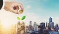 Saving money concepts, businessman hand putting coin in glass jar, with plant growing, city in sunrise background