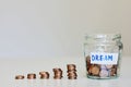Saving money for dream concept. Glass jar full of coins, stacks of coins and sign dream