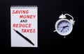 SAVING MONEY AND REDUCE TAXES is written in a white notepad near a white alarm clock on a black background