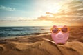 Saving money for summer vacation. Piggy bank with sunglasses on sandy beach near sea at sunset, space for text