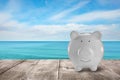 Saving money for summer vacation. Piggy bank on wooden surface near sea, space for text