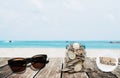 Saving money for vacation concept, glass coins container with sunglasses on wooden table at tropical beach