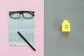 Savings account passbook, pen, glasses on pink background and yellow paper house on gray background Royalty Free Stock Photo