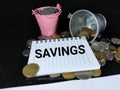 SAVINGS in black word on notebook with coins and buckets with black background.