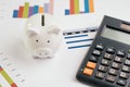 Savings and investment concept, white piggy bank with black calculator on pile or economic analysis report chart and graph on Royalty Free Stock Photo