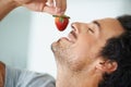 Savoring the sweetness. A gorgeous young man with head tilted back and holding a strawberry above his lips.