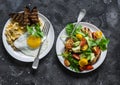 Savory breakfast - avocado, cherry tomatoes grilled bread salad and fried egg with hummus and rye croutons on dark background,