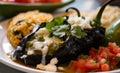 Savory close-up of Chiles Rellenos stuffed with queso fresco and herbs, served with a side of black beans and pico de gallo