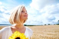 Savouring natures peace and tranquility. Smiling young woman standing in a wheat field and holding some sunflowers. Royalty Free Stock Photo