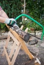 Sawing firewood manually with a hacksaw on a wooden sawhorse