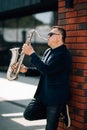 Saxophonist plays a golden saxophone on the street with passers-by in sight. spring. musical reed wind instrument