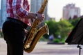 Saxophonist plays a golden saxophone on the street with passers-by in sight. spring. musical reed wind instrument. tongue wooden