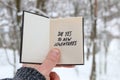 Say yes to new adventures on the background of the winter forest. Hand holding a book with the inscription. Royalty Free Stock Photo