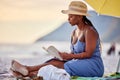 Saying no to the noise today. a beautiful young woman relaxing with a book at the beach. Royalty Free Stock Photo