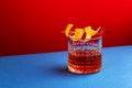 Sazerac cocktail with cognac, bourbon, absinthe, bitters, sugar and lemon peel. Dazzling red blue background with hard light and